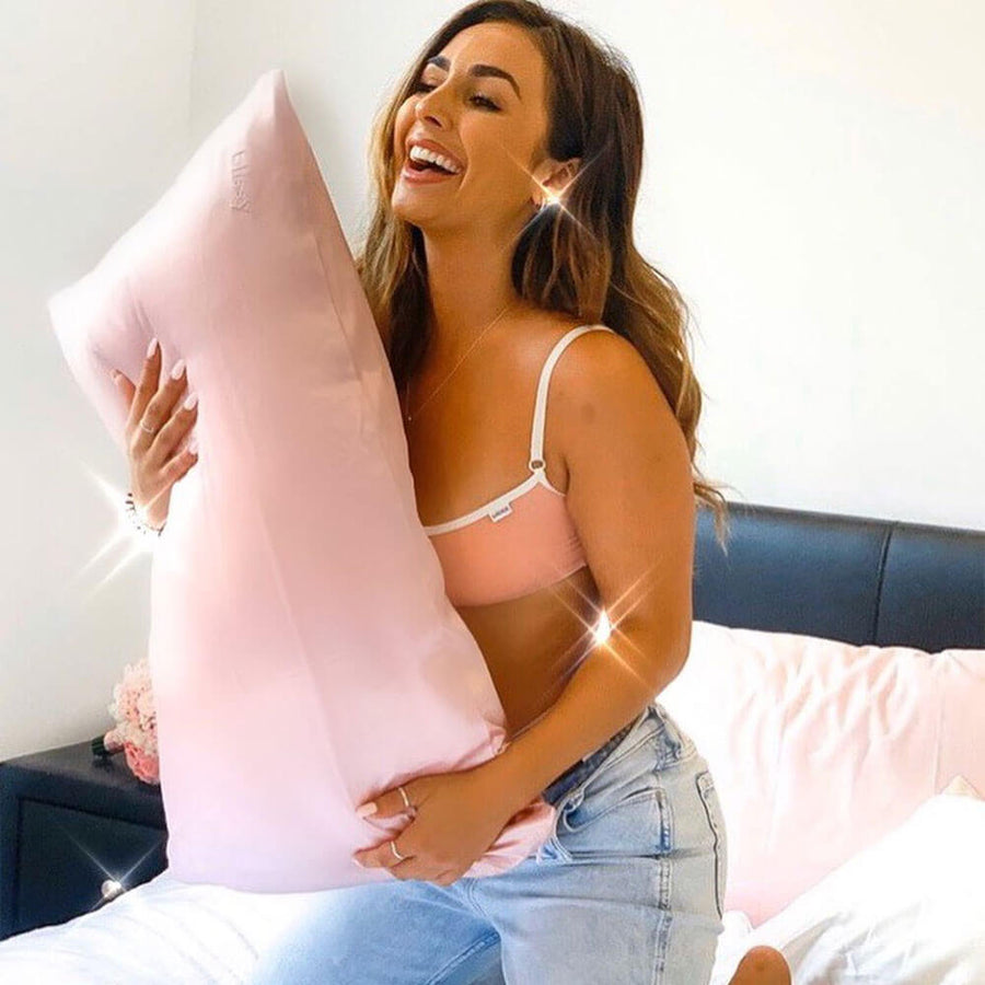 Woman smiling while hugging a pillow with Blissy mulberry silk pink pillowcase